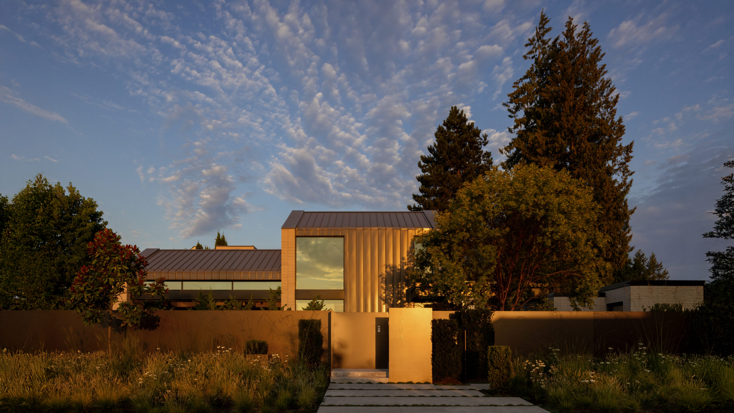 Modern office building at golden hour with metal siding, large glass windows, and surrounding trees in warm light.