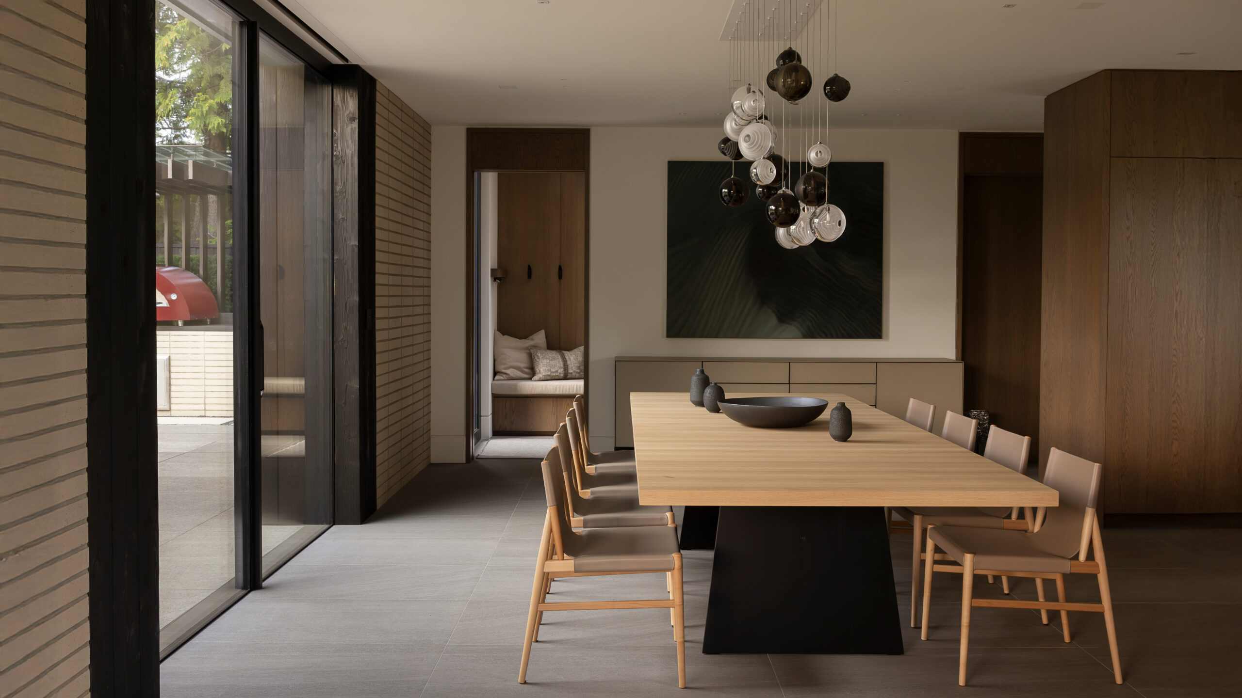 Modern dining room with a long wooden table, beige chairs, and a cluster of pendant lights overhead.